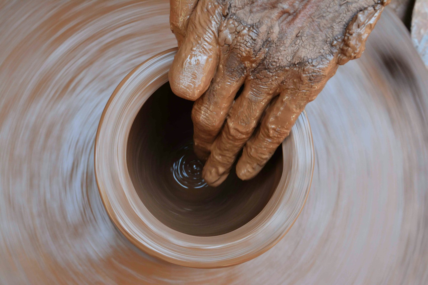 A potter's hands shaping a pot on a wheel